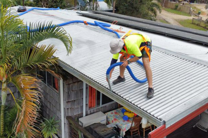 Trademan is high vis gear, working on roof, using vacuum gutter suction unit to remove leaves and twigs from metal gutter