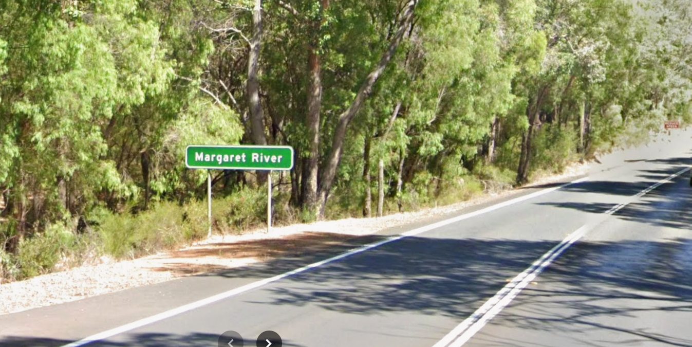 Margaret River town entrance sign beside a tree-lined road in Western Australia